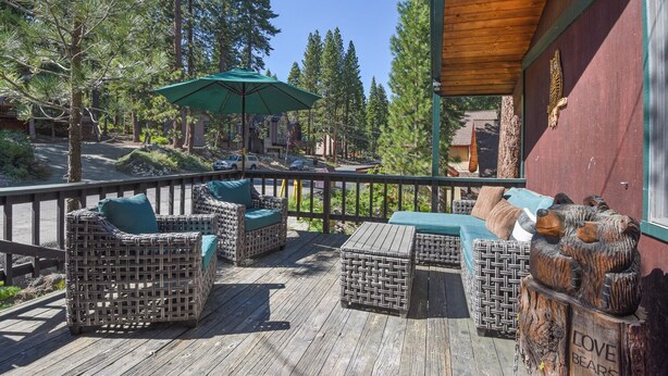 A wooden deck with wicker furniture and a green umbrella, surrounded by trees.
