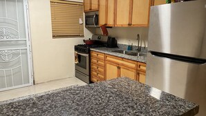 A kitchen with granite countertops, stainless steel appliances, wooden cabinets, and a stainless steel refrigerator. - Rolleville Darling House - 2 minute walk from the beach! (Exuma)