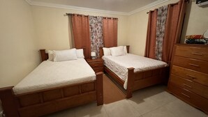 A bedroom with two wooden beds, a nightstand, a dresser, and a window with curtains. - Rolleville Darling House - 2 minute walk from the beach! (Exuma)