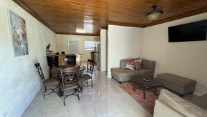 A living room with a dining area, a sofa, a coffee table, and a kitchen in the background. - Rolleville Darling House - 2 minute walk from the beach! (Exuma)