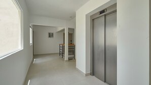 A corridor with a stainless steel elevator, a small kitchen area with stools, and a window providing natural light. - Modern Studio in Crisfer Monthly Stays WiFi & AC (Punta Cana)