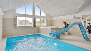 An indoor swimming pool with a slide, a hot tub, and large windows. - Nice home in Blåvand with sauna (Blåvand)
