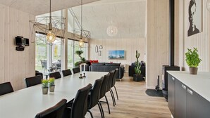 A modern kitchen with a large dining table, black chairs, pendant lights, and wooden paneling. - Nice home in Blåvand with sauna (Blåvand)