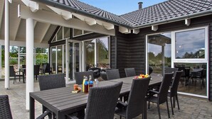 An outdoor patio with a table set for dining, surrounded by chairs, and a grill. - Nice home in Blåvand with sauna (Blåvand)