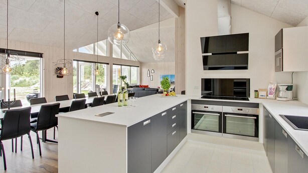 A modern kitchen with a large island, built-in ovens, and a dining area with a view of the outdoors. - Nice home in Blåvand with sauna (Blåvand)