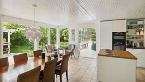 Una cocina moderna con una isla central, armarios blancos y vistas al jardín a través de amplios ventanales.