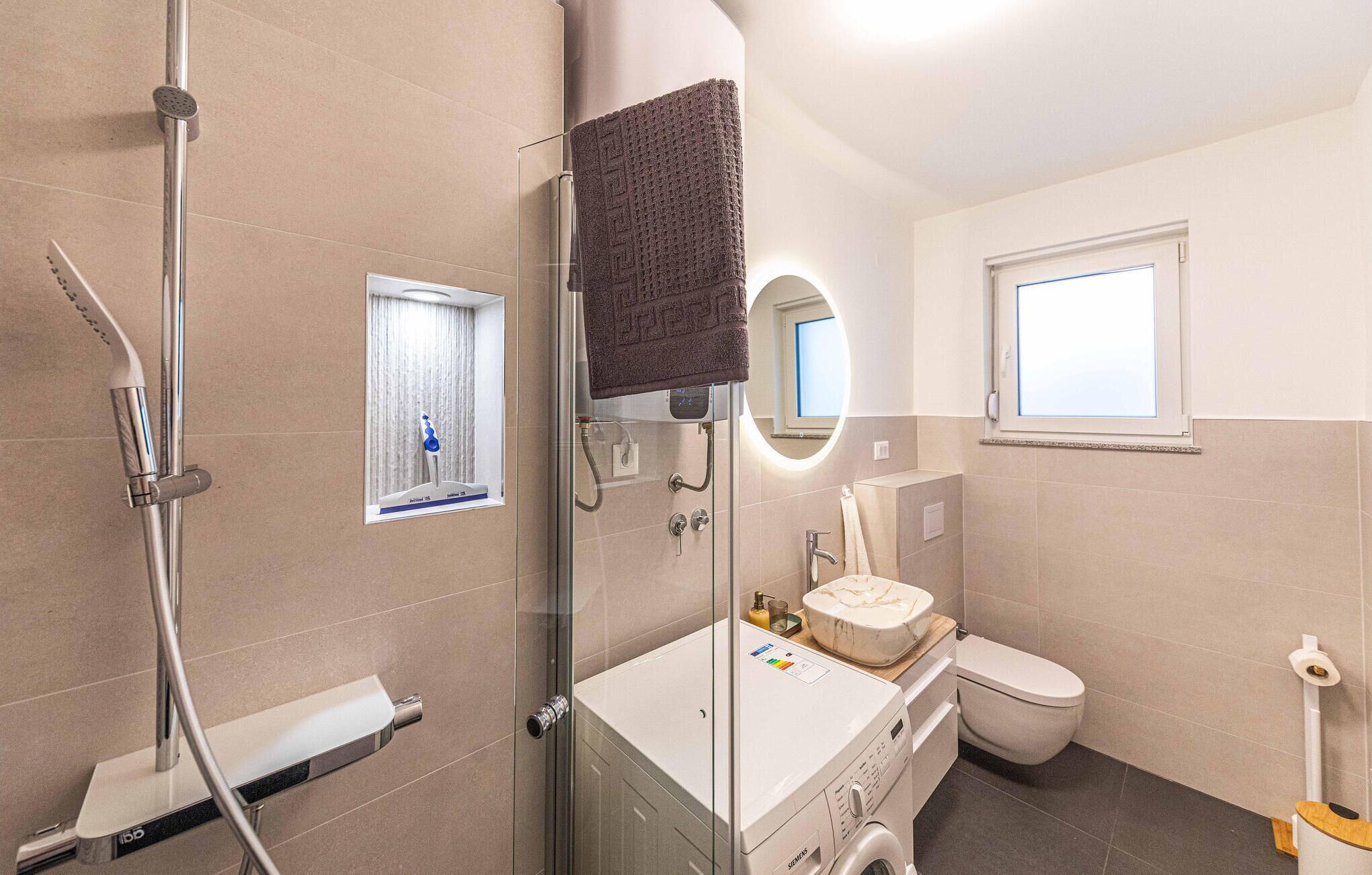 Een moderne badkamer met een douchecabine van glas, een toilet en een wasmachine.