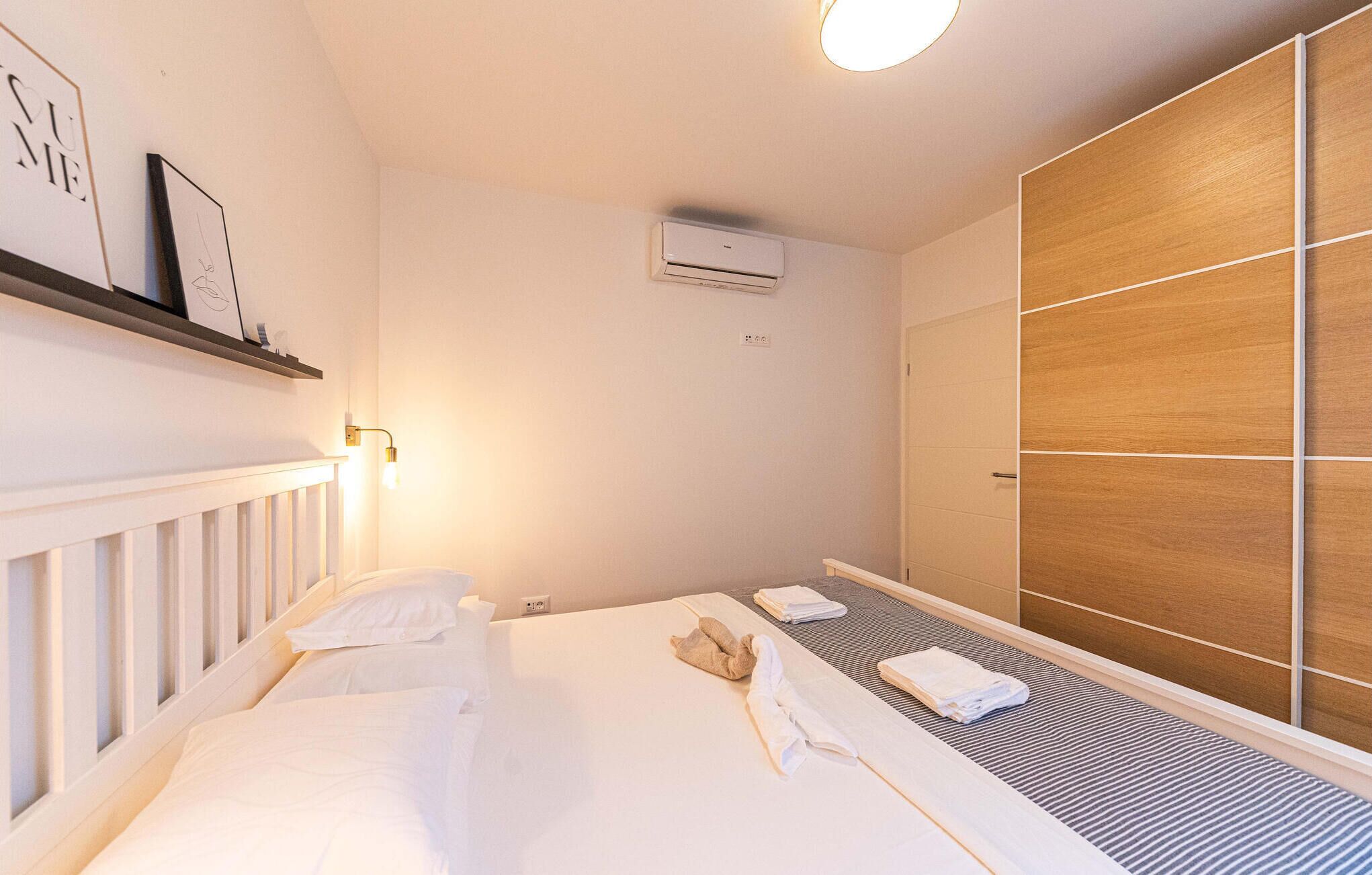 Une chambre d’hôtel comprenant un lit, une lampe de chevet, un appareil de climatisation, une armoire et une étagère avec des photos encadrées.