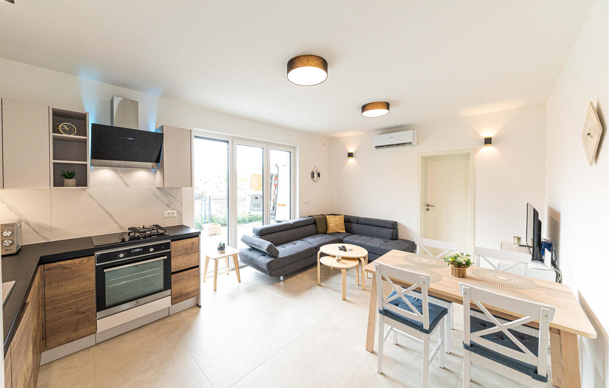A modern kitchen with a built-in stove, a dining area with a wooden table and chairs, and a grey sectional sofa.
