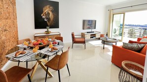 Un salon moderne comprenant un coin repas, une grande fenêtre offrant une vue sur la ville et une œuvre d’art représentant le visage d’un lion, accrochée au mur.