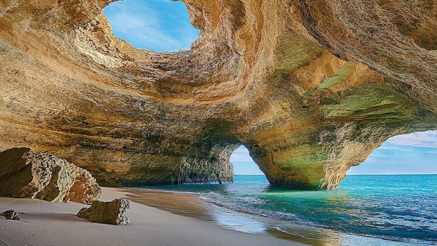 Une formation rocheuse naturelle dotée d’une ouverture circulaire, une plage de sable et une eau d’un bleu cristallin.