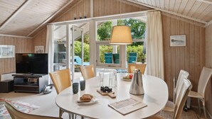 Une pièce chaleureuse avec une table à manger ronde, des chaises, un téléviseur et une grande fenêtre avec des rideaux.