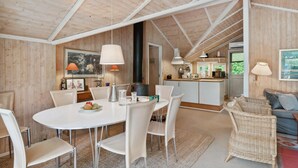 Une cuisine spacieuse dotée d’appareils électroménagers modernes, un coin repas avec une table ronde et des chaises, et un coin salon confortable avec un fauteuil en osier et un canapé.