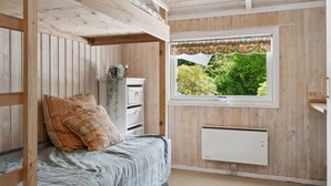 Une pièce confortable avec un lit superposé, une petite armoire blanche, une fenêtre ornée d’un rideau à motifs floraux et un radiateur.