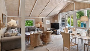Un salon confortable avec un canapé, des fauteuils en osier, un téléviseur et un coin repas comprenant une table et des chaises.