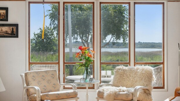 A room with a view of a lake, two wicker chairs, a table with a vase of flowers, and a fluffy chair. - Nice home in Orø with house sea view (Orø)