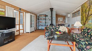 A cozy living room with a television, a glass-top coffee table, a sofa, and a bookshelf. - Nice home in Orø with house sea view (Orø)
