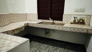 A compact kitchen with a sink, a window with a wooden shutter, and a patterned backsplash. - Aathil Guest House (Nilaveli)