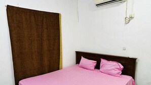 A single bed with a wooden headboard, a brown curtain, and a white wall with an air conditioning unit. - Aathil Guest House (Nilaveli)