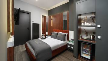 A modern hotel room with a large bed, built-in wardrobe, bedside tables, a minibar, and a TV.