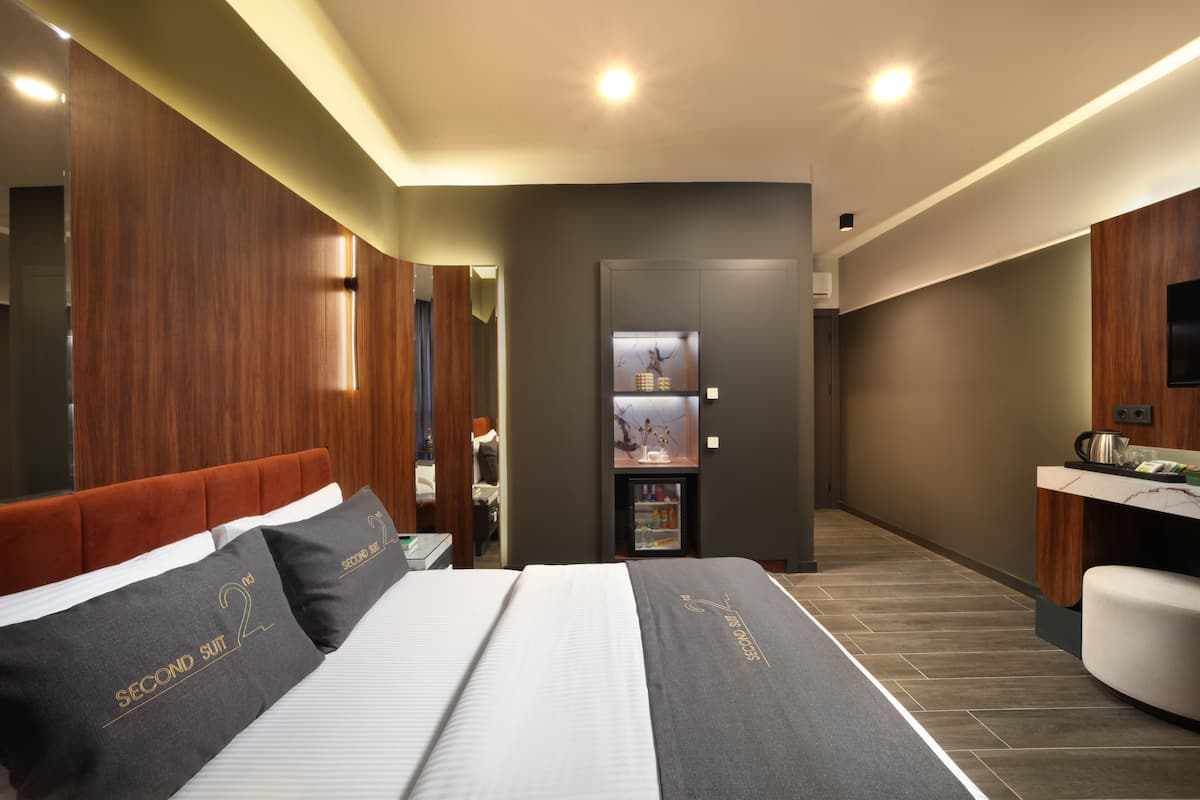 Moderni hotellihuone, jossa on suuri sänky, puinen pääty, pieni keittokomero ja peili seinällä.