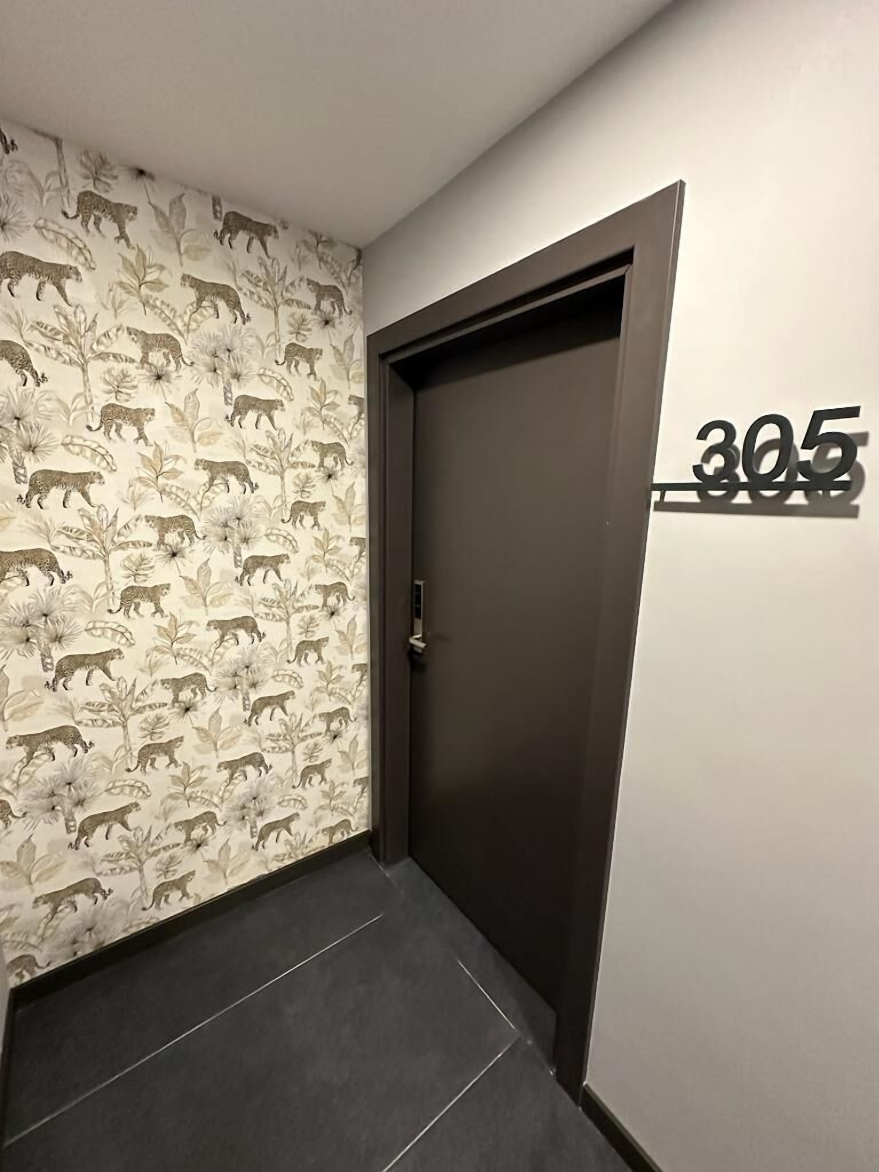A hallway with a door marked '305', a patterned wallpaper with animal prints, and a dark floor.