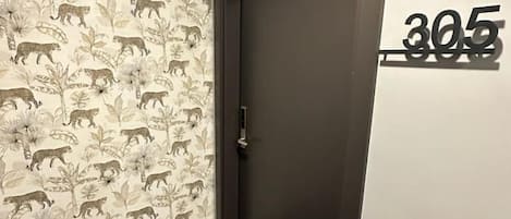 A hallway with a door marked '305', a patterned wallpaper with animal prints, and a dark floor.