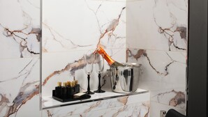 Un baño con suelo de mármol, una botella de champán siendo abierta, dos copas y un cubo para champán.