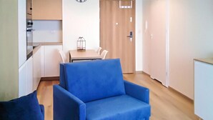 Quarto com poltrona azul, mesa de jantar com cadeiras, cozinha e porta com puxador.