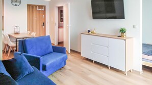 Uma sala de estar moderna com um sofá azul, um armário branco e uma TV de tela plana fixada na parede.