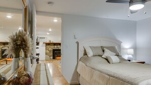 Un dormitori amb un llit, una taula de nit, una làmpada i vista a una zona d'estar amb una llar de foc.