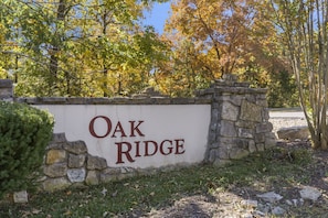 A sign reading "Oak Ridge" with a stone wall and trees in the background.