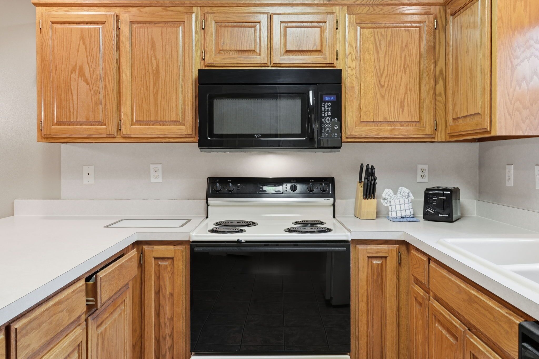 A kitchen with wooden cabinets, a black microwave, a white stove, and a toaster.