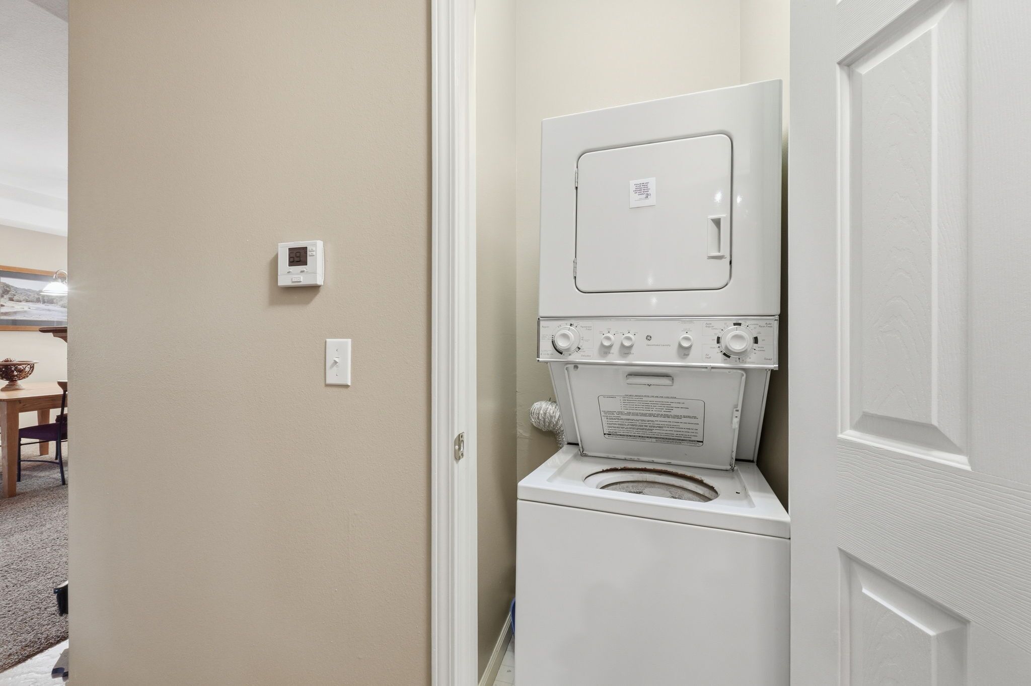 A compact laundry room with a washer and dryer, a thermostat on the wall, and a door leading to another room.