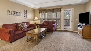 A living room with a red sofa, a wooden coffee table, a TV stand, and a ceiling fan. - Charming StoneBridge Village Condo - Gated Community (Reeds Spring)