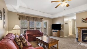 A living room with a sofa, coffee table, TV, fireplace, and a ceiling fan. - Charming StoneBridge Village Condo - Gated Community (Reeds Spring)