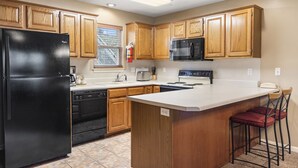 A kitchen with wooden cabinets, a black refrigerator, a microwave, and a sink. - Charming StoneBridge Village Condo - Gated Community (Reeds Spring)