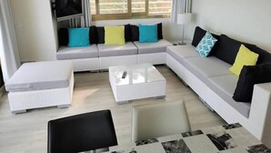 Een moderne woonkamer met een modulaire bank, een glazen salontafel en een flatscreen televisie aan de muur.