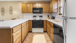 A kitchen with wooden cabinets, a white countertop, a microwave, a stove, and a dishwasher. - Unique, Connecting Condo & Suite in StoneBridge Village (Reeds Spring)