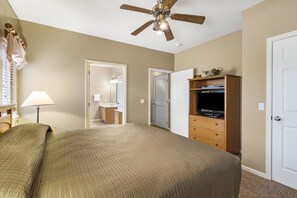 A bedroom with a bed, a ceiling fan, a TV, a dresser, and a door.