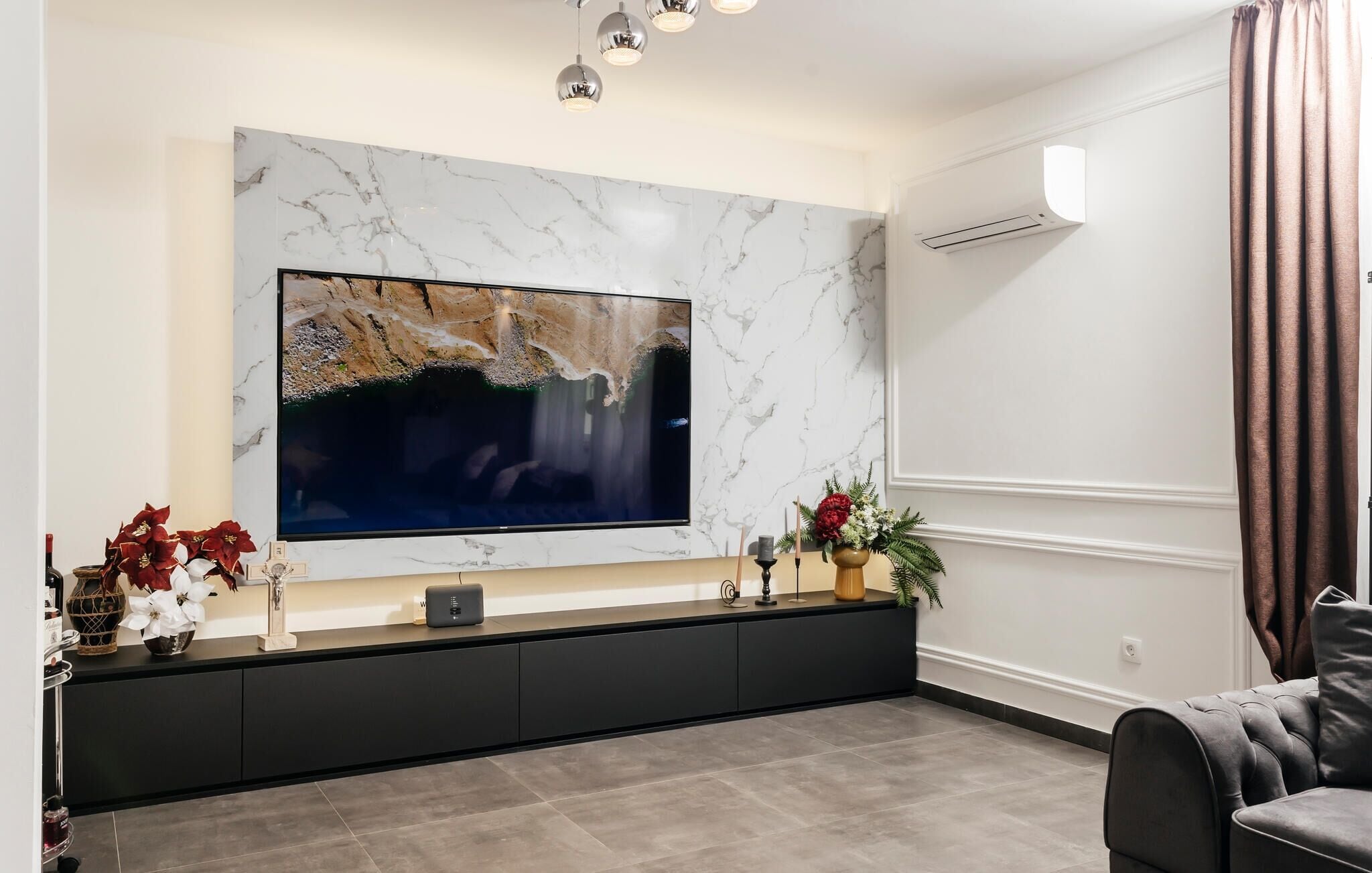 A modern living room with a large flat-screen TV mounted on a marble wall, a dark console table, and a grey sofa.