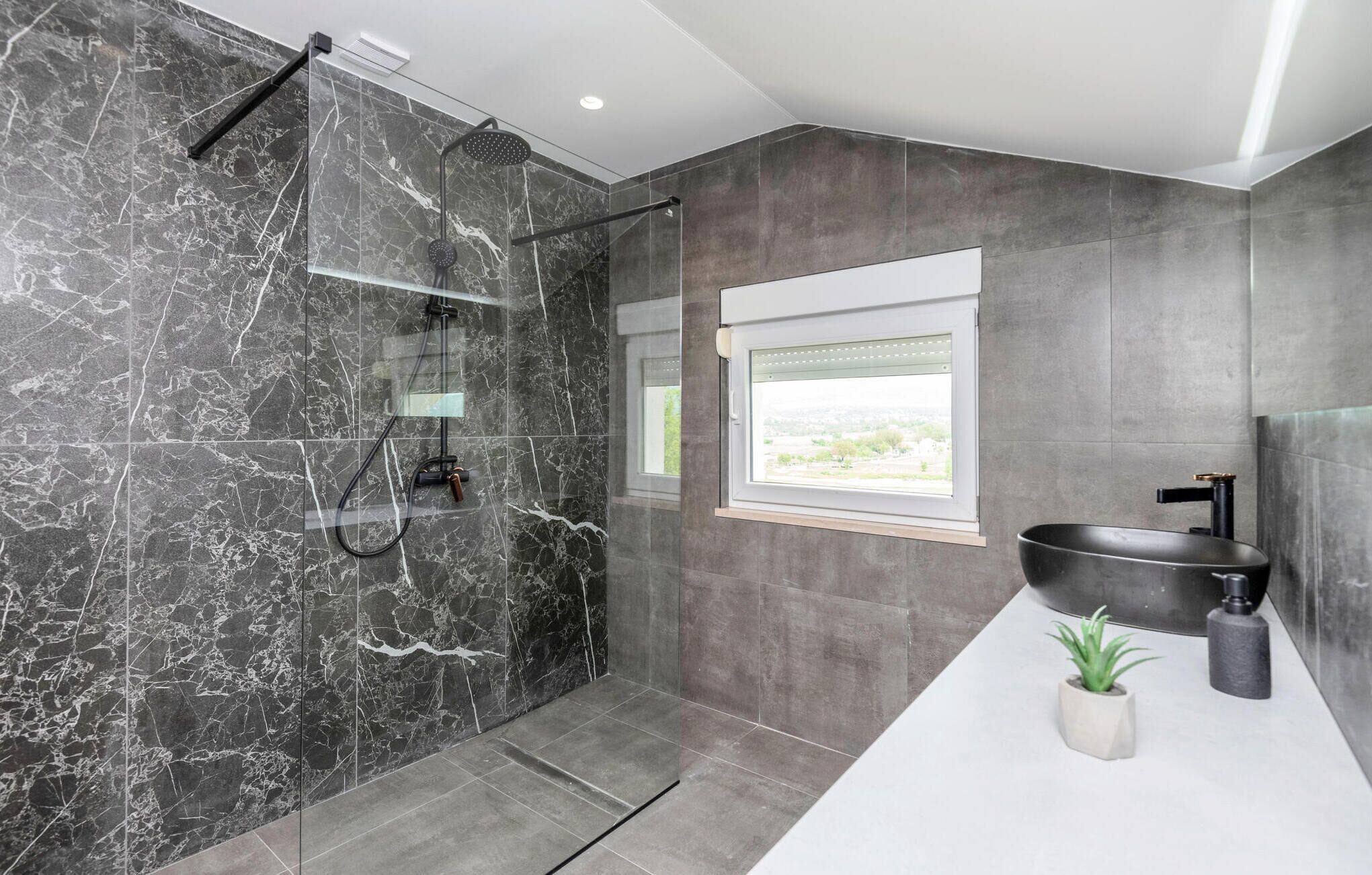 A modern bathroom with a glass-enclosed shower, a large sink, and a window providing a view.