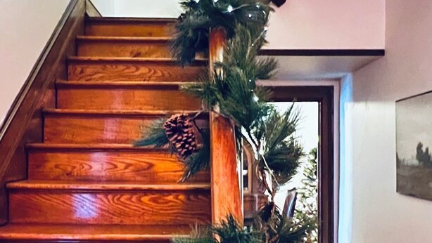 A wooden staircase with a decorative arrangement of pine branches and a pine cone on a wooden stand. - Spacious Historic Home: 4 bedrooms, 2.5 bath (New Oxford)