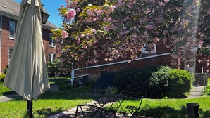 A patio area with a table and chairs, a hanging umbrella, and a blooming tree. - Spacious Historic Home: 4 bedrooms, 2.5 bath (New Oxford)
