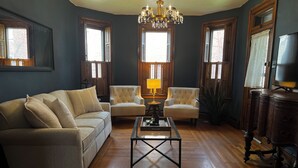 Een woonkamer met een bank, twee fauteuils, een salontafel, een kroonluchter en houten vloeren.