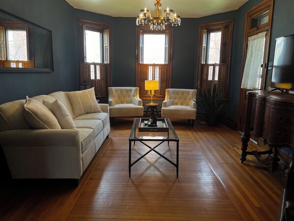 A living room with a sofa, two armchairs, a coffee table, a chandelier, and wooden floors. - Spacious Historic Home: 4 bedrooms, 2.5 bath (New Oxford)
