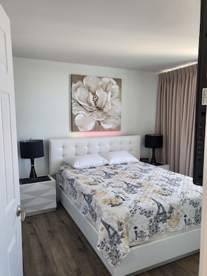 Ein Schlafzimmer mit einem großen Bett, zwei Nachttischen, einem Wandbild und einem Fenster mit Vorhängen.