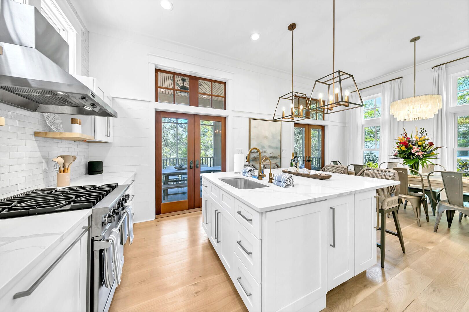 Une cuisine moderne avec des meubles blancs, un grand îlot central doté d’un évier et un coin repas offrant une vue agréable.