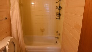 A small, wooden-paneled bathroom with a toilet, shower, and bathtub.