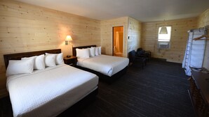 A wooden-paneled room with two beds, a desk, a chair, and a dresser.